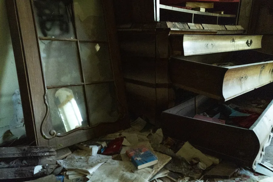 An abandoned room with broken furniture, an overturned drawer and papers across the floor