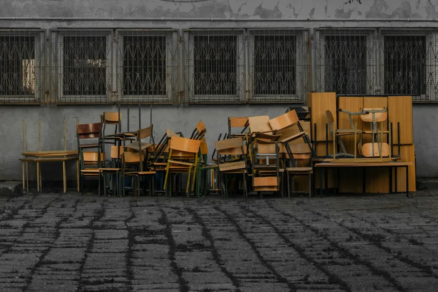 Rows of old wooden chairs stacked outside a building