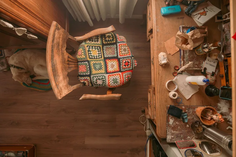 Household clutter spread across a wooden floor: an upturned chair, tools, kitchenware and loose odds and ends