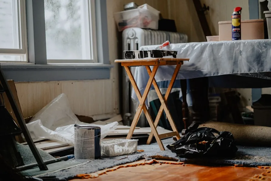 A room part-way through a cleanout, with bagged rubbish, paint cans, a folding table and loose building debris