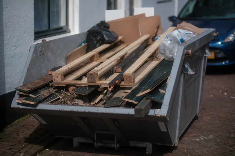 A skip parked at a kerb, filled with broken lumber and renovation debris
