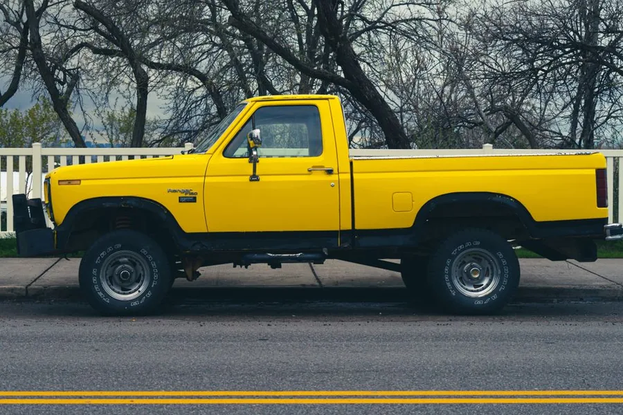 An older yellow pickup truck with an open bed, parked at the roadside