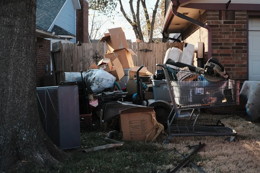 A pile of discarded boxes, furniture and household debris heaped beside a brick house