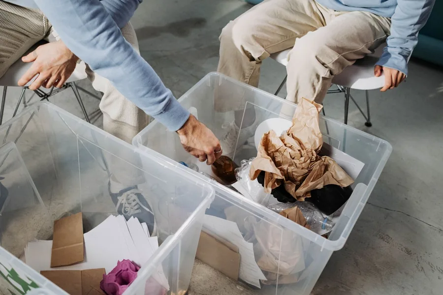 Two people sorting household items into clear plastic storage bins on a floor